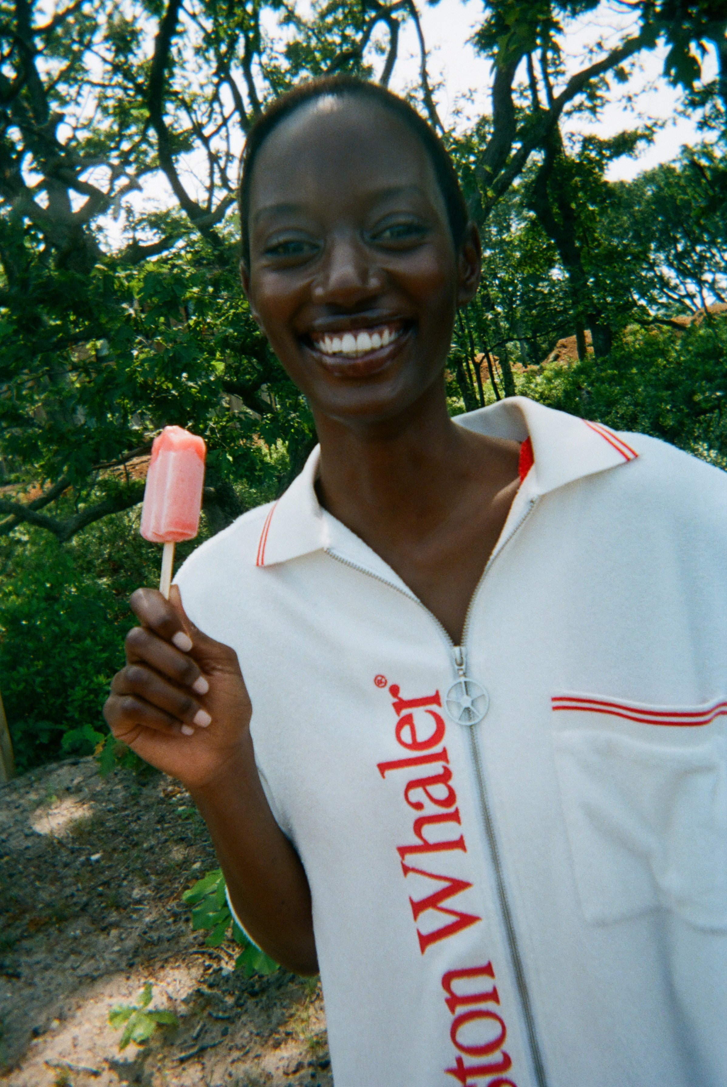 Woman wearing the white terry 'Whaler' Cabana, holding a popsicle and has a smile on her face. 
