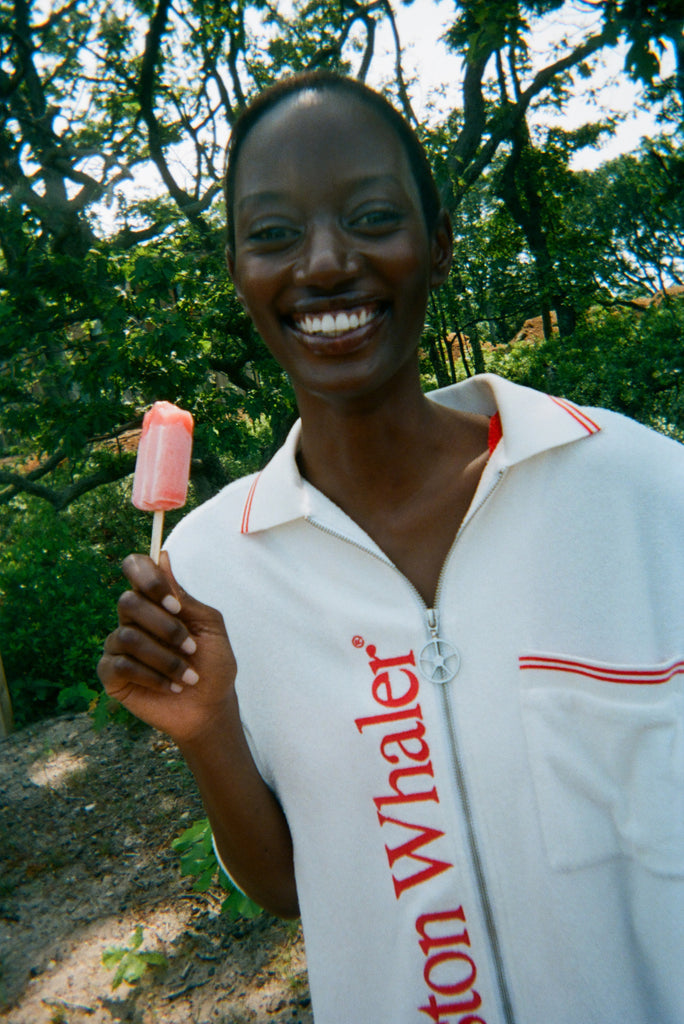 Woman wearing the white terry 'Whaler' Cabana, holding a popsicle and has a smile on her face. 