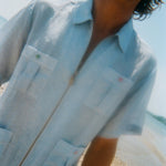 Man wearing a light blue short-sleeve zip-up shirt with four front pockets. Each pocket features a red or green button.