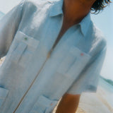 Man wearing a light blue short-sleeve zip-up shirt with four front pockets. Each pocket features a red or green button.