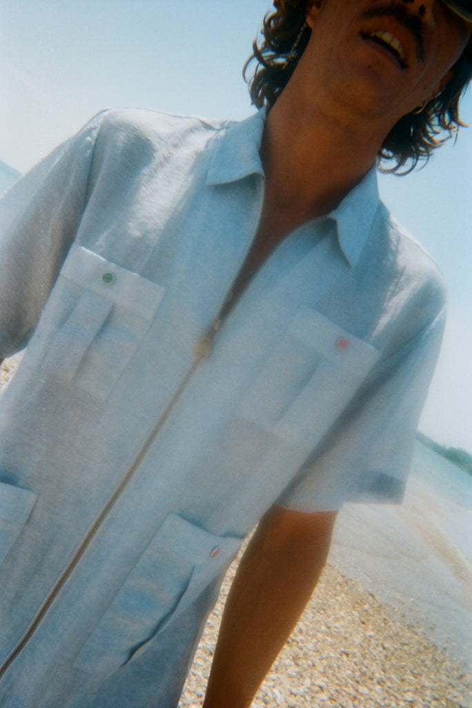 Man wearing a light blue short-sleeve zip-up shirt with four front pockets. Each pocket features a red or green button.