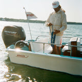 A man standing on a boat in a rain jacket and matching shorts with tan trim. He wears a white cap with red 'Whaler' text.