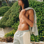 shirtless man wearing Tombolo oyster shirts looks off into distance, holding the linen oyster shirt over his left shoulder