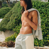 shirtless man wearing Tombolo oyster shirts looks off into distance, holding the linen oyster shirt over his left shoulder
