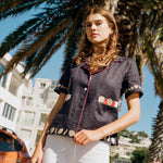 Female model wearing the crop cut vongole top with white pants in front of a palm tree