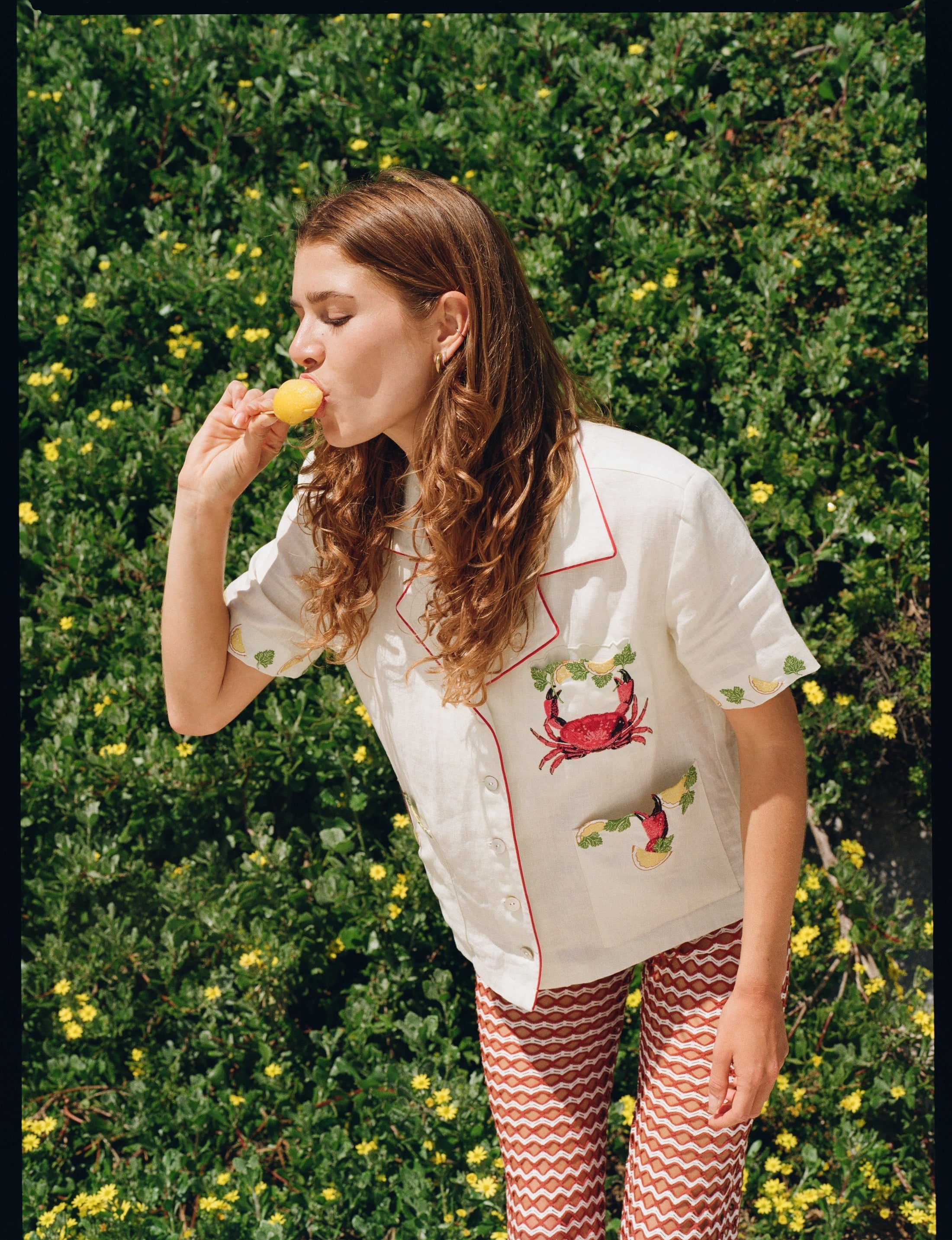 Woman eating ice cream leaning forward against hedge backdrop
