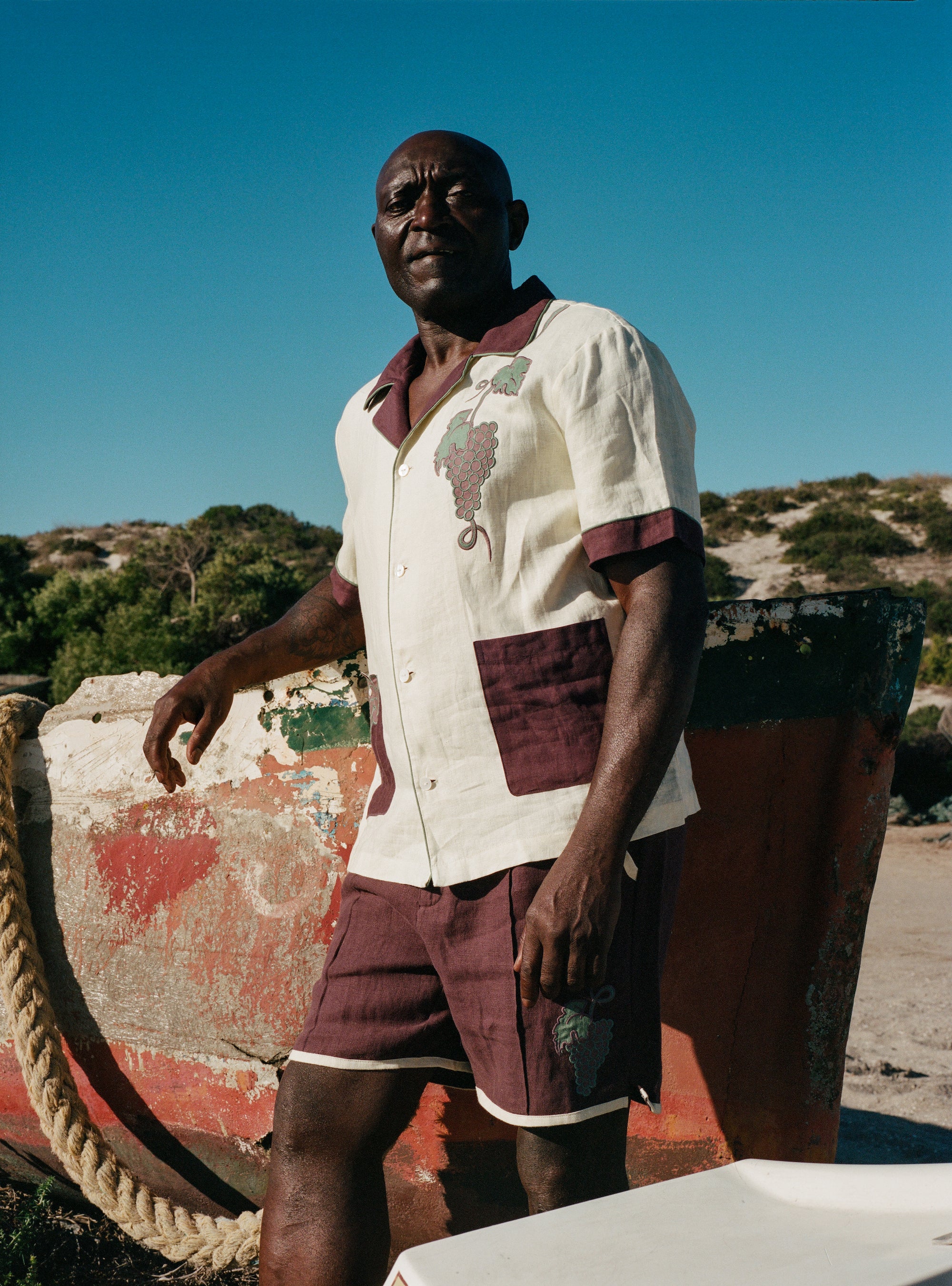 Male model in full 'Tombarolo' Cabana set leaning against a dry-docked boat.