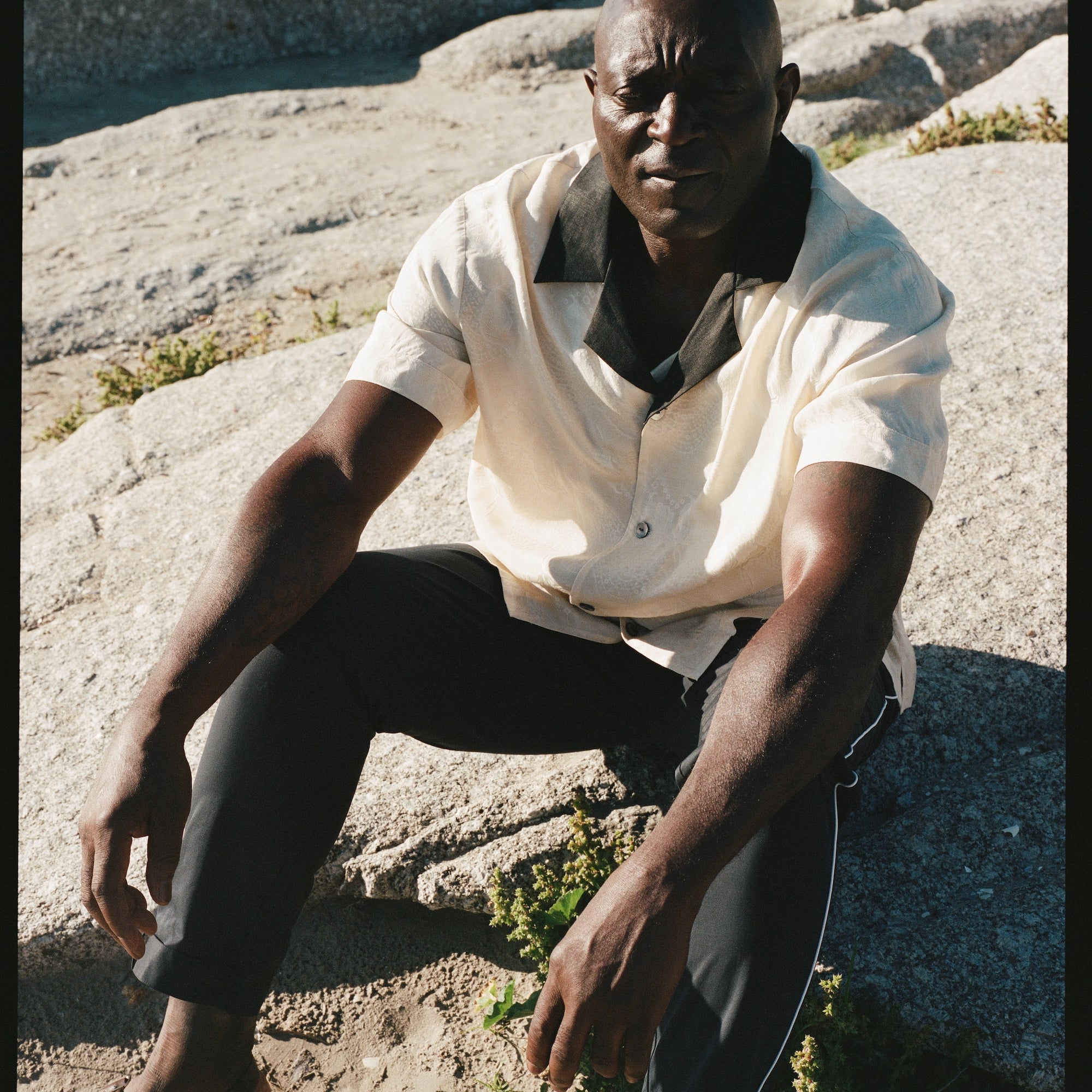 Male model wearing the cabana with the navy traveler pants sitting on a rock