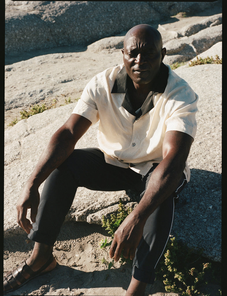 Male model wearing the cabana with the navy traveler pants sitting on a rock