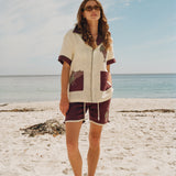 Female model standing on beach wearing full 'Tombarolo' cabana set with sunglasses on and brown leather sandals
