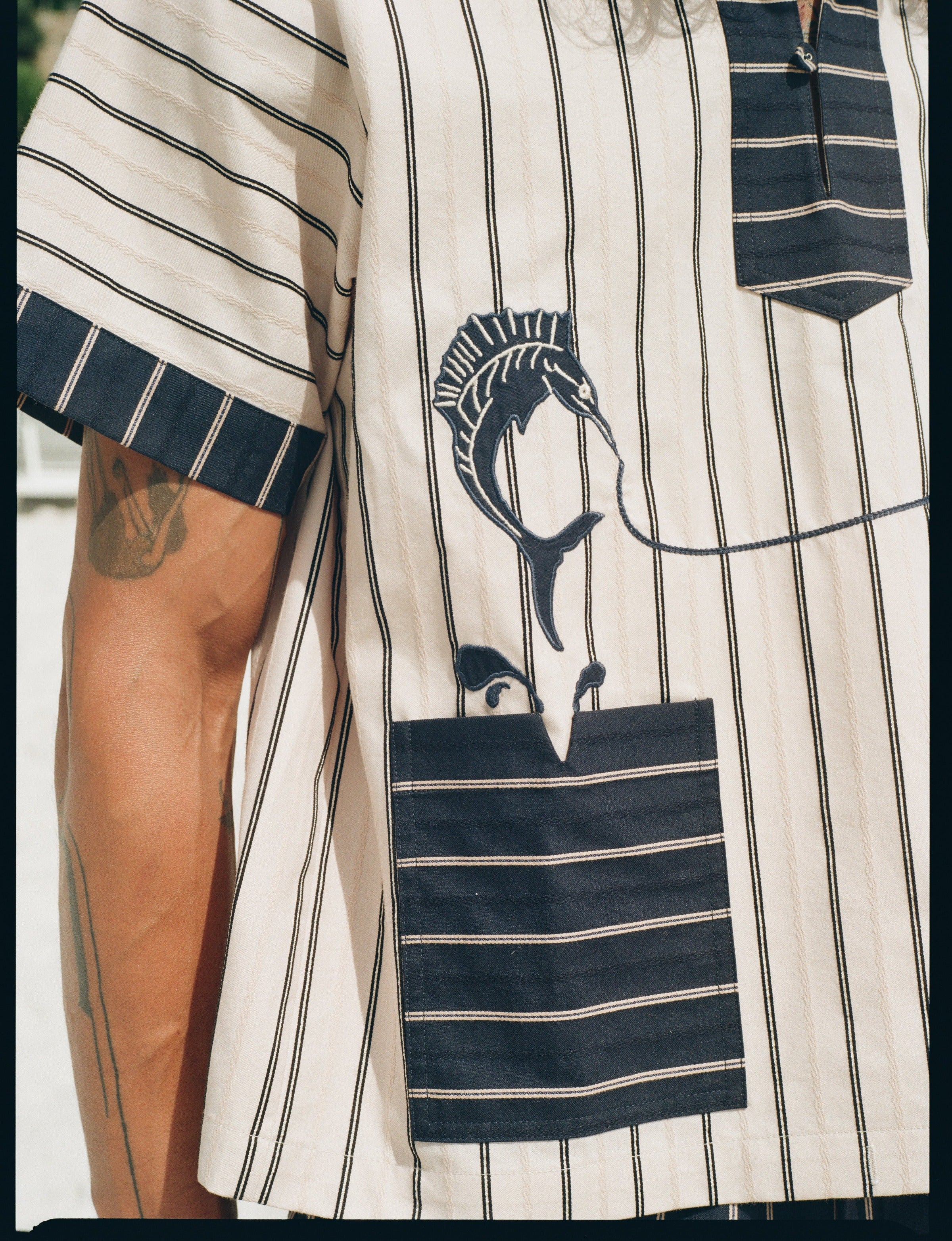 close-up of model in Tombolo striped pop-over shirt navy sleeve and pocket detailing with swordfish shown
