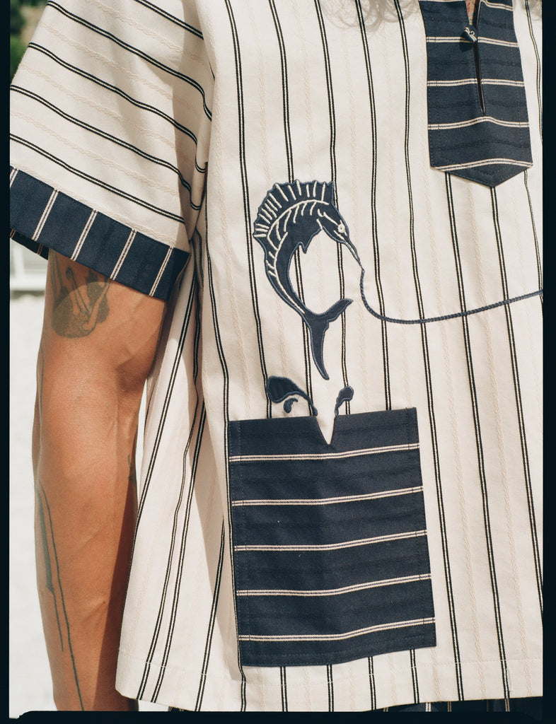 close-up of model in Tombolo striped pop-over shirt navy sleeve and pocket detailing with swordfish shown