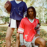 A man and woman seen wearing the blue mesh football jersey and the red mesh football jersey, standing in a park. 