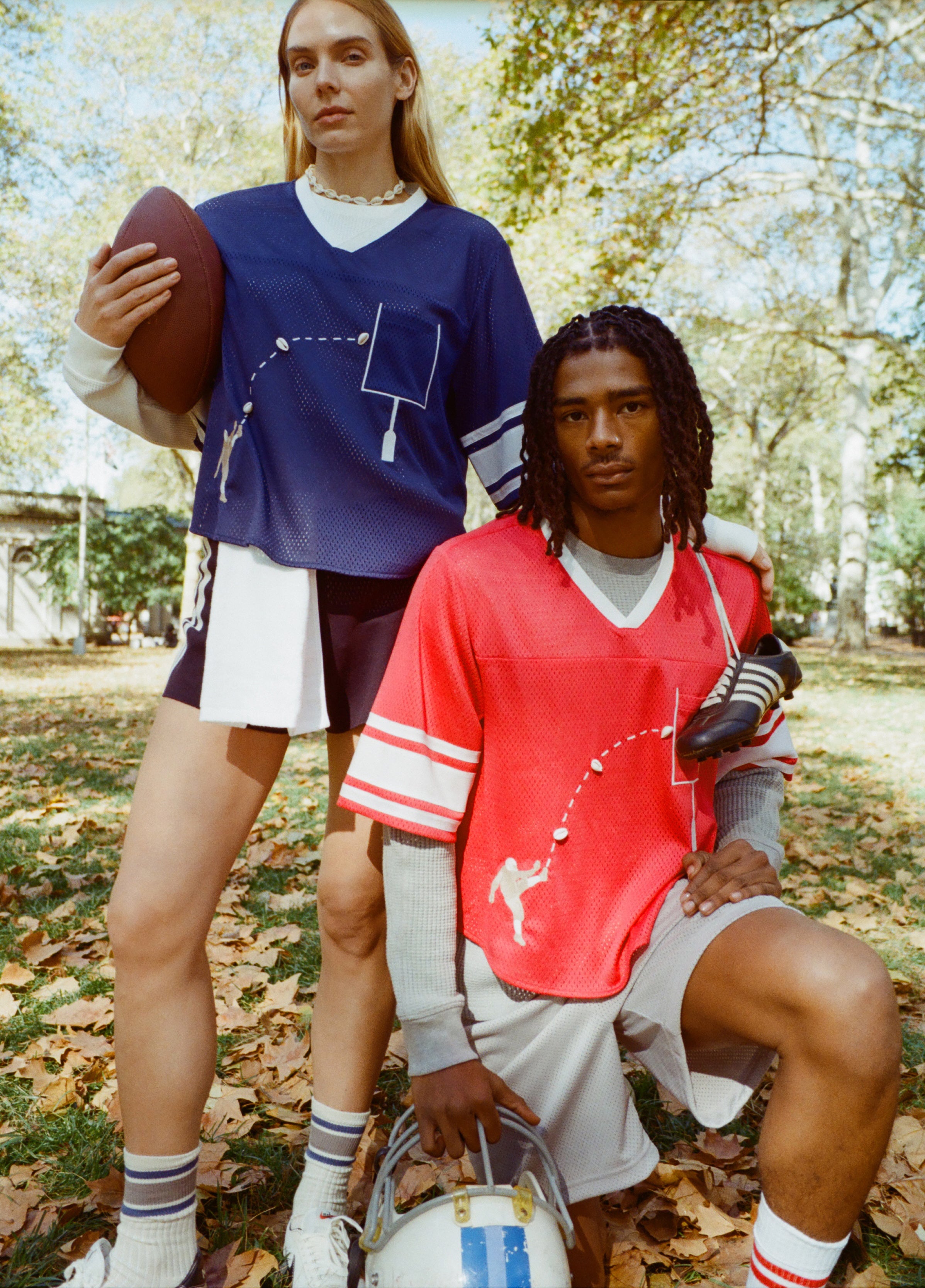 A man and woman seen wearing the blue mesh football jersey and the red mesh football jersey, standing in a park. 