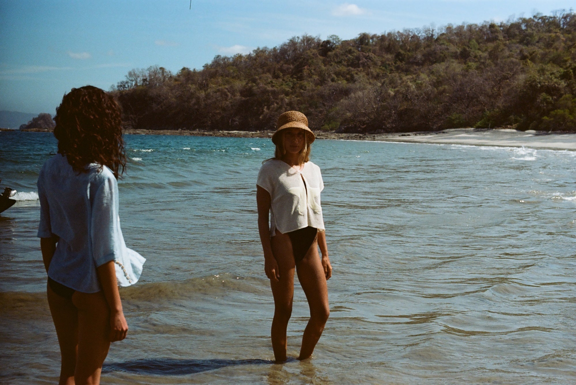 Woman standing ankle deep in ocean, wearing 'Starfish Strut' Hand Towel Top with a black swimsuit underneath and a straw hat.