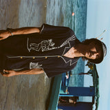Sideways image of male model with longer hair and a mustache wearing the full 'Agua Magica' Cabana Set while standing ankle deep in the ocean. 