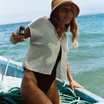 Woman wearing the 'Starfish Strut' Hand Towel Top over a black one piece bikini. She is holding a disposable camera in her right hand while she is moving on a boat. 