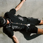 Male model laying on the beach wearing the full 'Agua Magica' Cabana set, with the bucket hat rest over his face to block the sun.