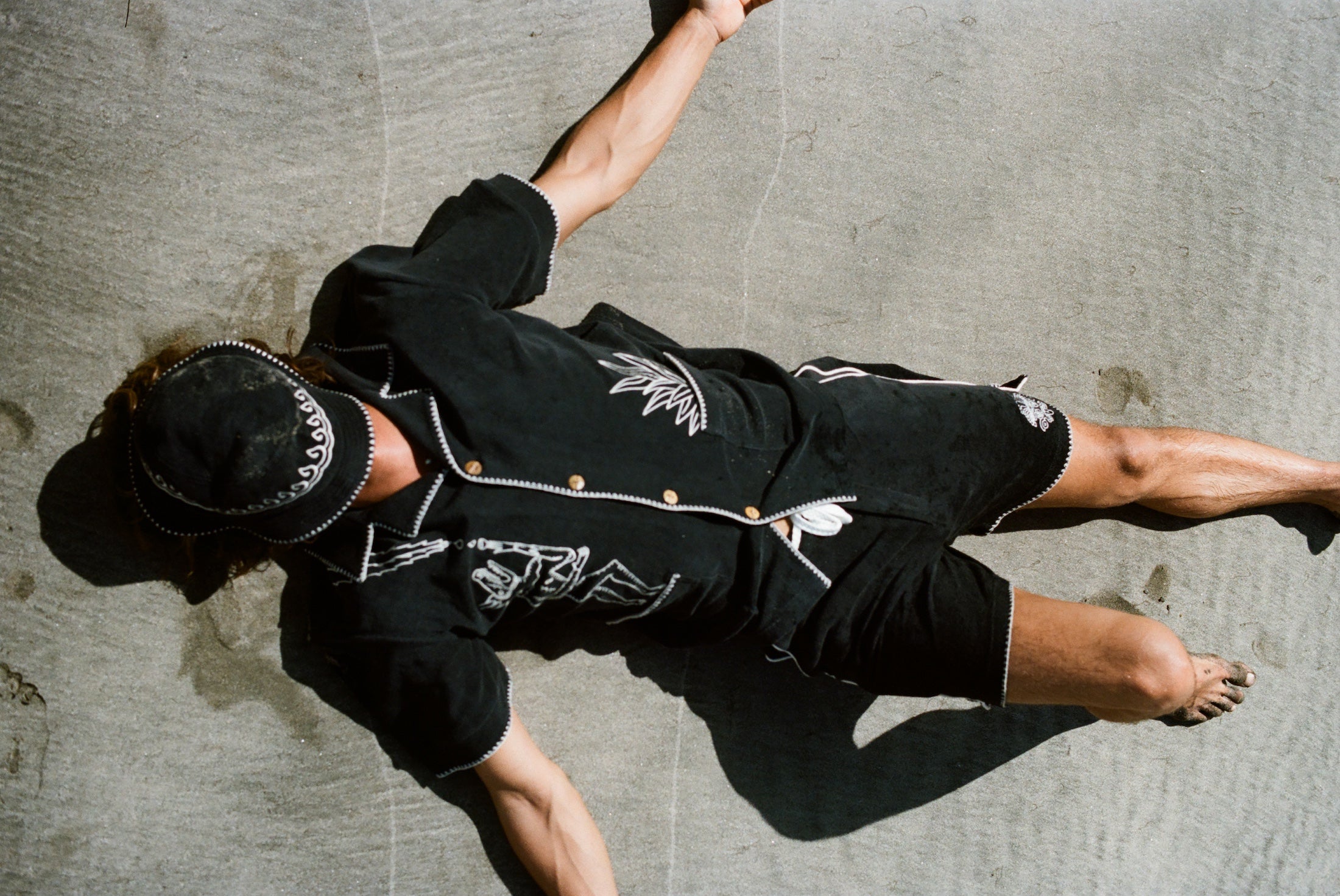 Image of male model lying in the sand with the full 'Agua Magica' Cabana Set on. He has his arms spread out and the bucket hat covering his face from the sun.