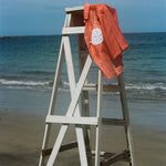 Orange sand dollar bikini shirt pictured hanging off an empty lifeguard stand at the beach.