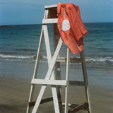 Orange sand dollar bikini shirt pictured hanging off an empty lifeguard stand at the beach.