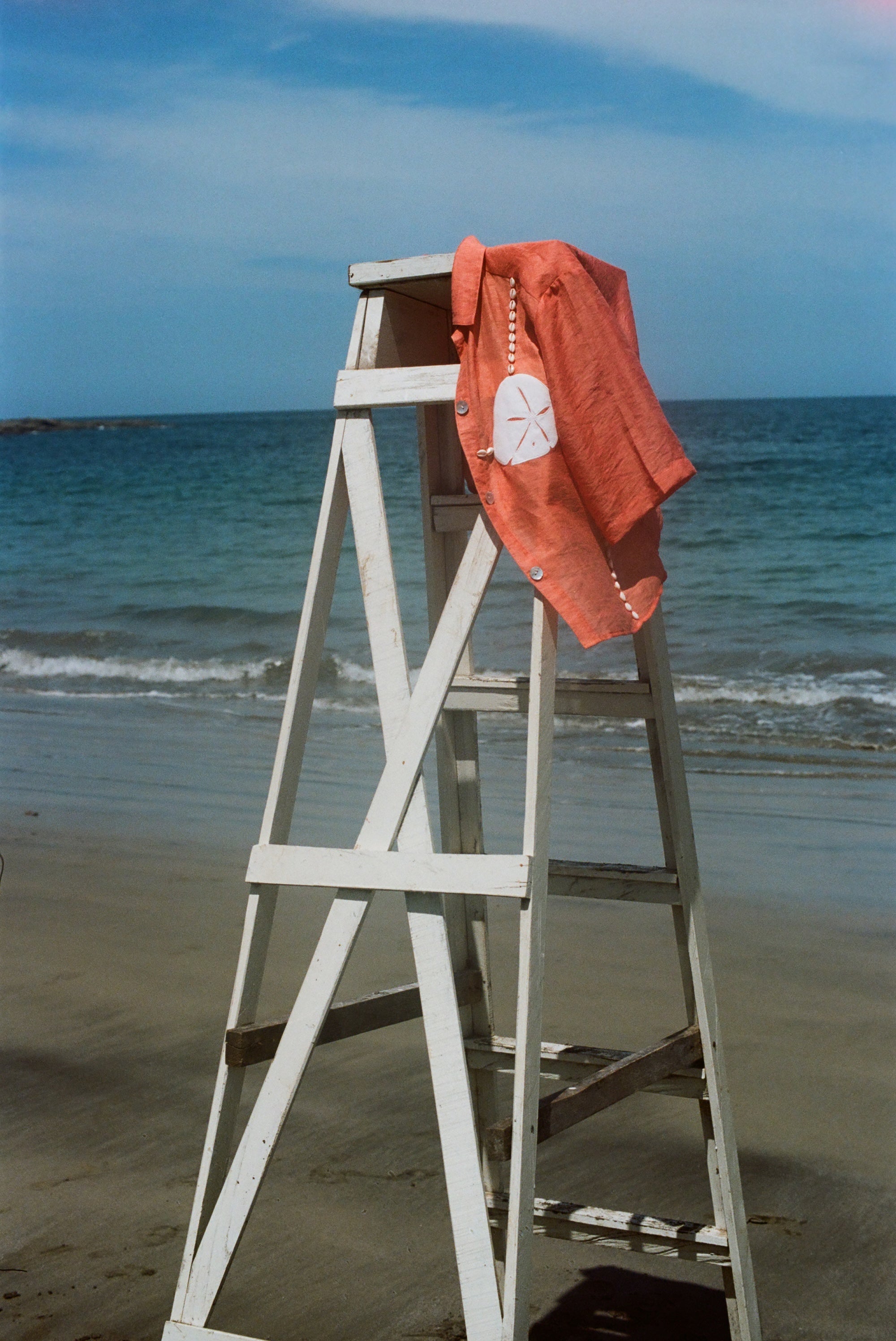 Orange sand dollar bikini shirt pictured hanging off an empty lifeguard stand at the beach.