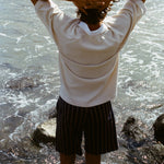 Image of a man's backside, wearing the beige mesh 'TomPolo' with striped shorts and has his hands behind his head. 