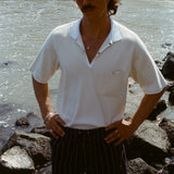 Man standing on a rocky beach, wearing the striped Easy-Shorts and our beige mesh 'Tompolo'.