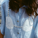 Close-up of a woman standing near the ocean wearing  light blue sand dollar bikini shirt.