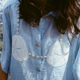 Close-up of a woman standing near the ocean wearing  light blue sand dollar bikini shirt.