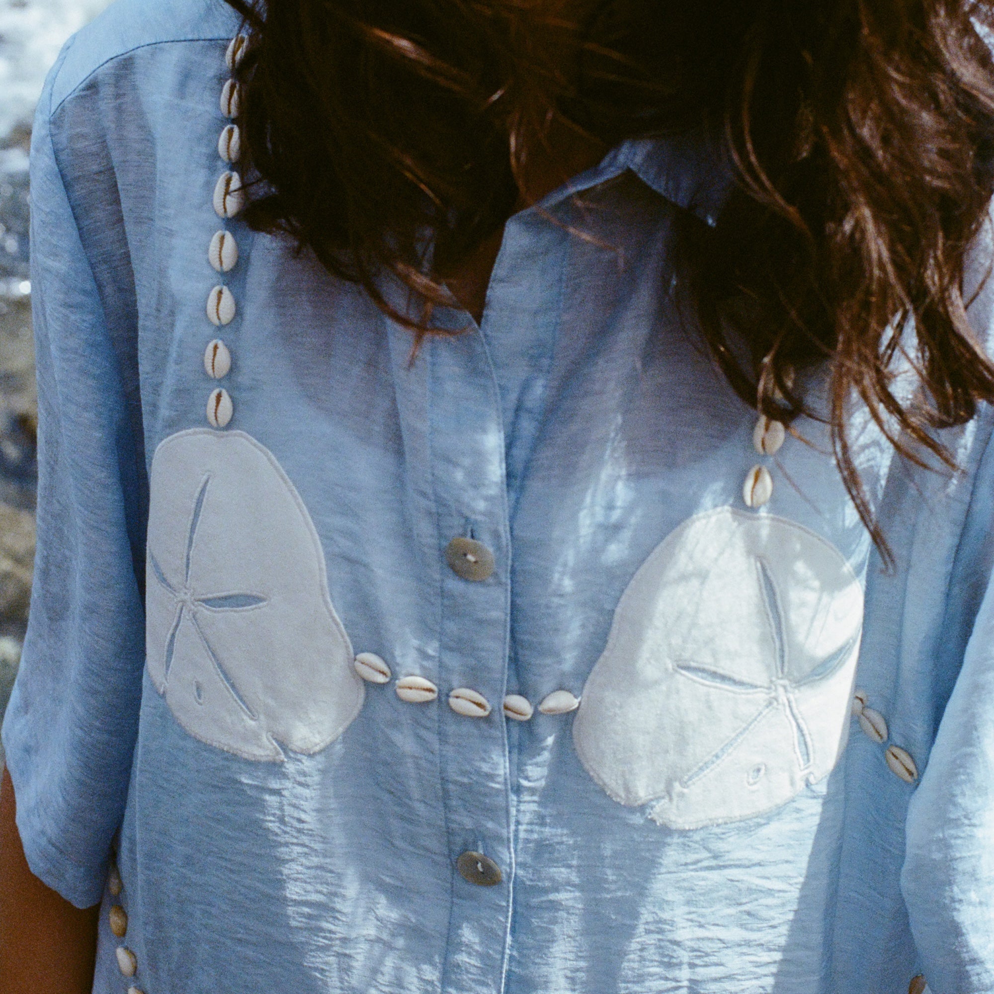 Close-up of a woman standing near the ocean wearing  light blue sand dollar bikini shirt.