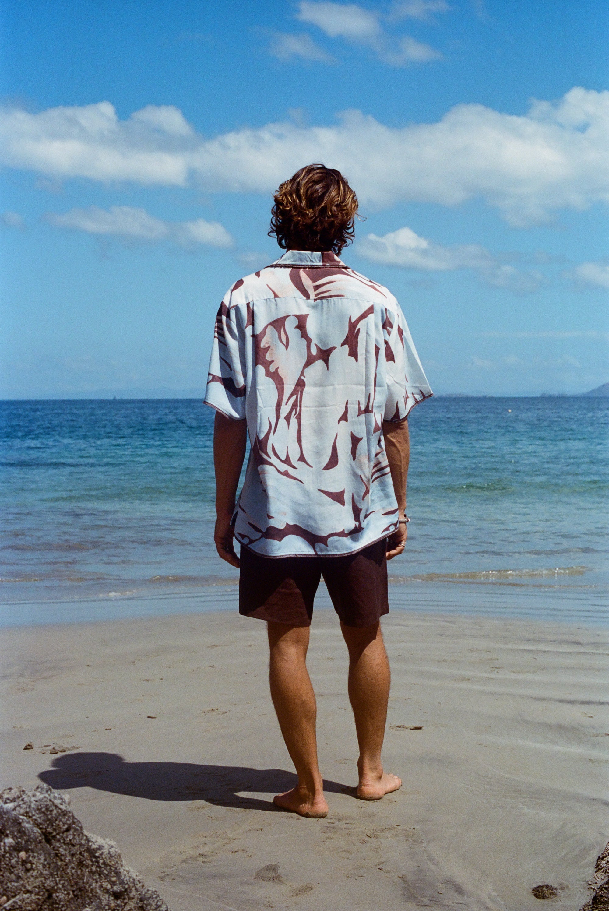 Image from behind of man on beach wearing the 'Mary Ball x Tombolo' Shirt with brown linen Easy Going Shorts.
