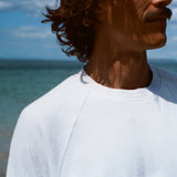Zoomed in image of the collar of our white terry tee, modeled by a brunette man standing on the beach.