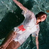 Woman floating in a pool wearing a white button-down shirt with embroidered fries in a red gingham pocket and fry detailing on the sleeves.