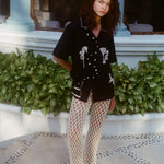 Female model wearing the 'Tip Your Bartenders!' Cabana with cream-colored open-knit pants with black sandals.