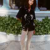Female model wearing the 'Tip Your Bartenders!' Cabana with cream-colored open-knit pants with black sandals.
