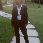 Man wearing the Easy-Going Tuxedo Jacket, untied bow tie, and relaxed black drawstring pants, standing barefoot.