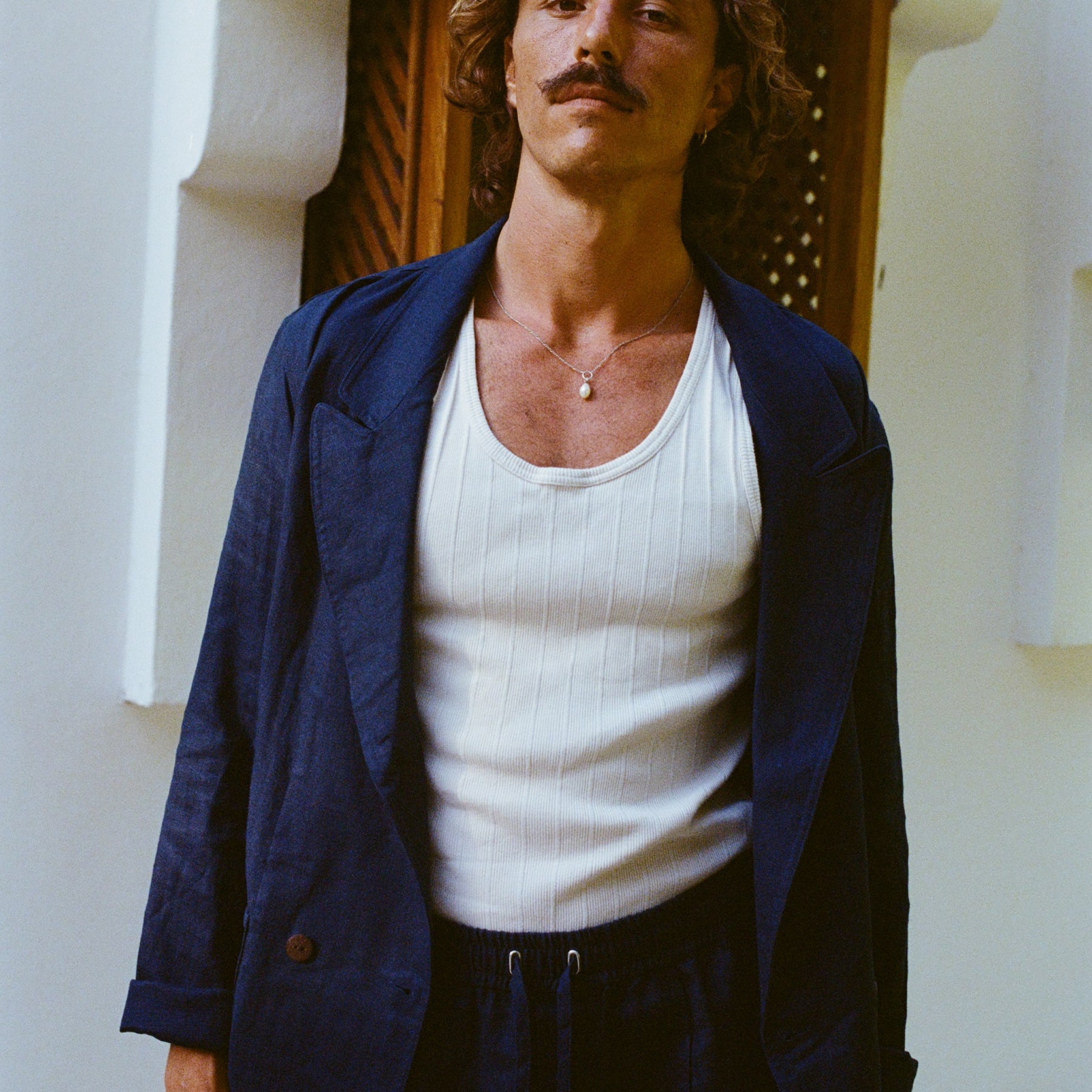 Man standing wearing the full linen navy suit, with a white tank underneath. Jacket is fully open. 