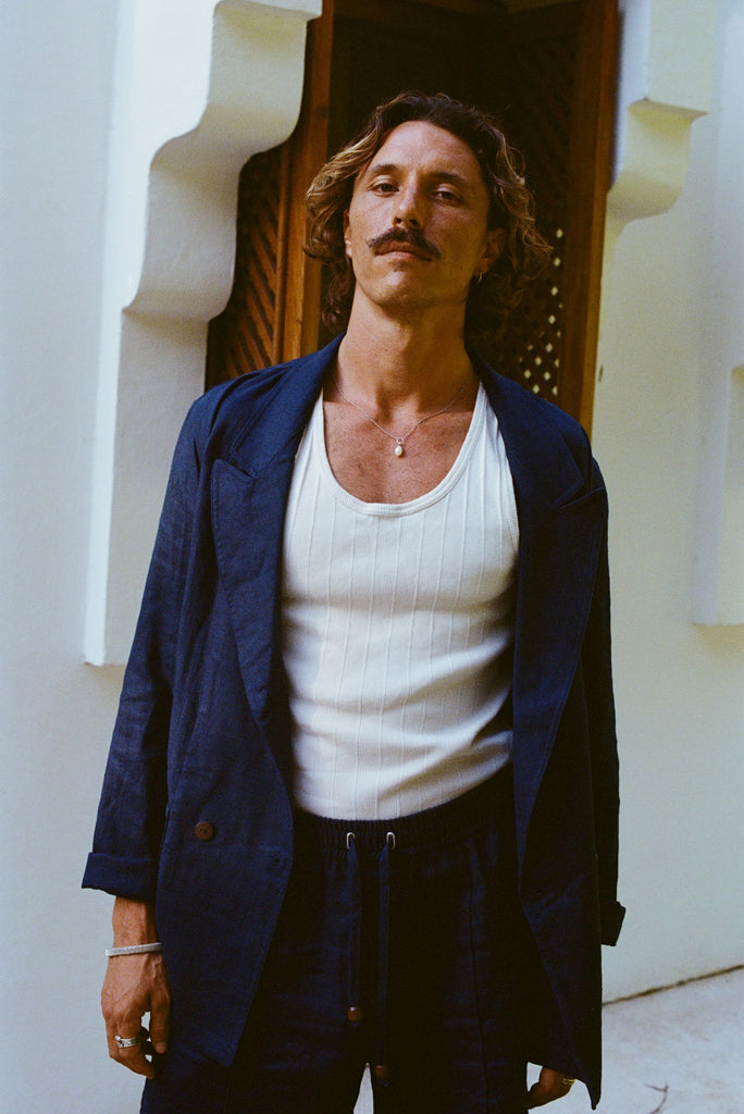 Man standing wearing the full linen navy suit, with a white tank underneath. Jacket is fully open. 