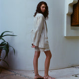 Woman standing in a courtyard wearing a sand-colored linen blazer and matching shorts.