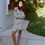 Brunette woman standing in the full Easy Going Linen Suit in Sand with black sandals. She has her arms wrapped around herself.
