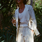 Brunette man with a glass of wine while wearing a sand linen Easy Going Suit Jacket with sand linen matching shorts, and a while tank top underneath. 