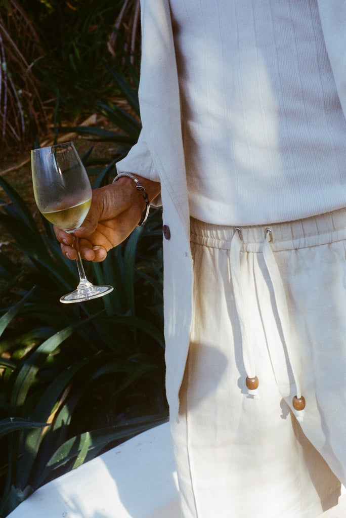 Close-up of man wearing the sand linen shorts while holding a glass of white wine. 