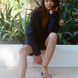 Woman sitting outside wearing the Easy Going Navy Linen Shorts and the matching Jacket and black sandals. 