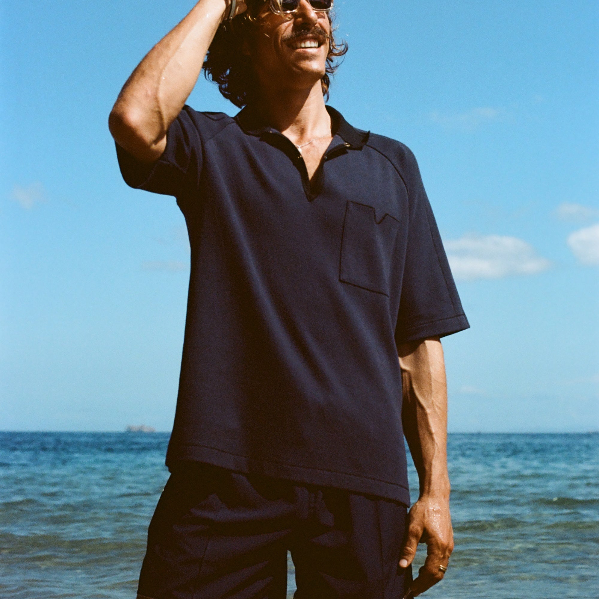 Man posed on the beach wearing navy 'TomPolo' with our navy Cabrisa swim trunks.