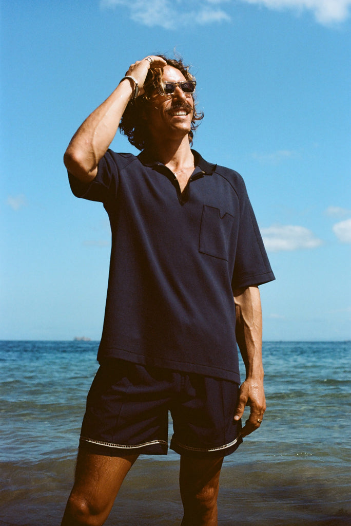 Man posed on the beach wearing navy 'TomPolo' with our navy Cabrisa swim trunks.