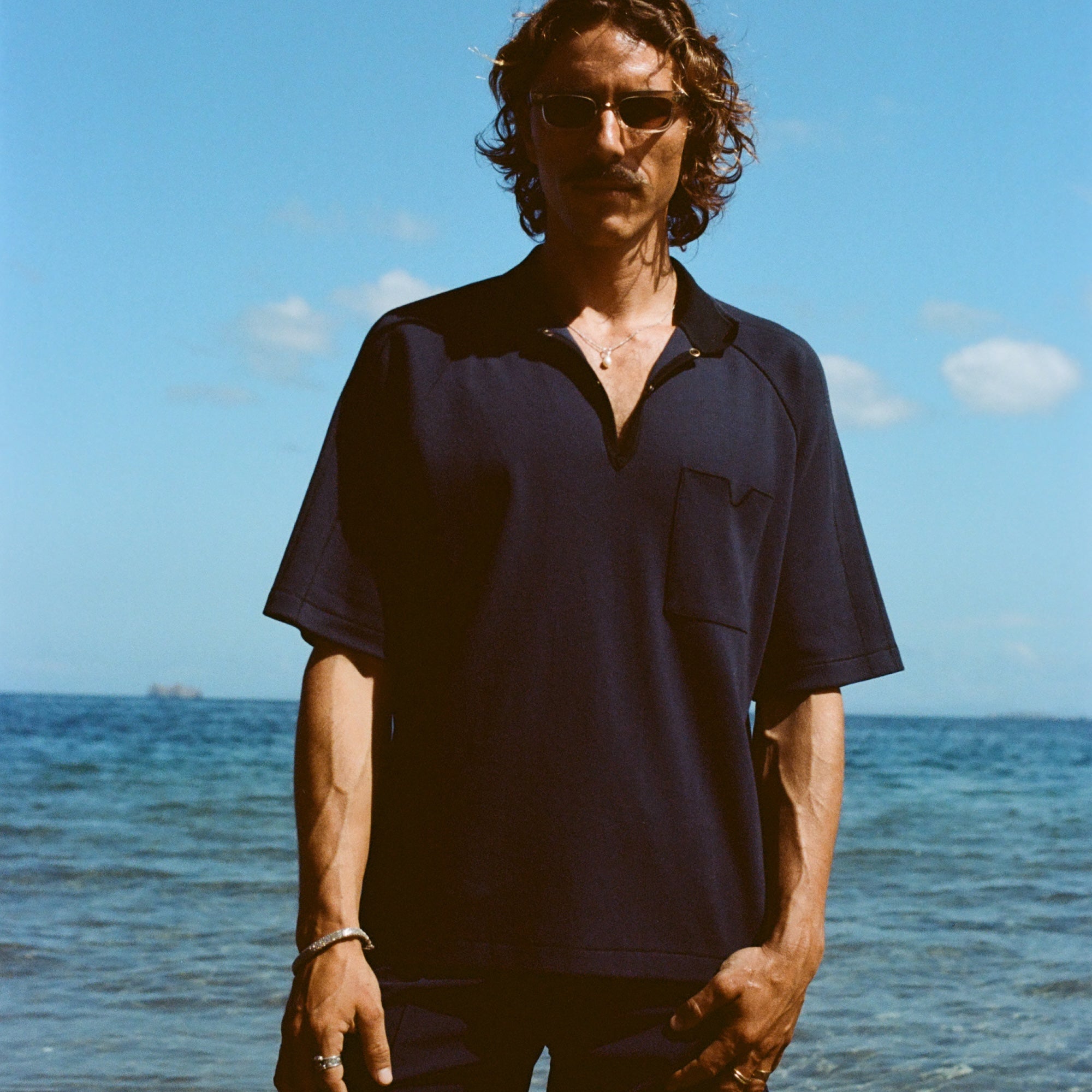 Man posed on the beach wearing navy 'TomPolo' with our navy Cabrisa swim trunks.