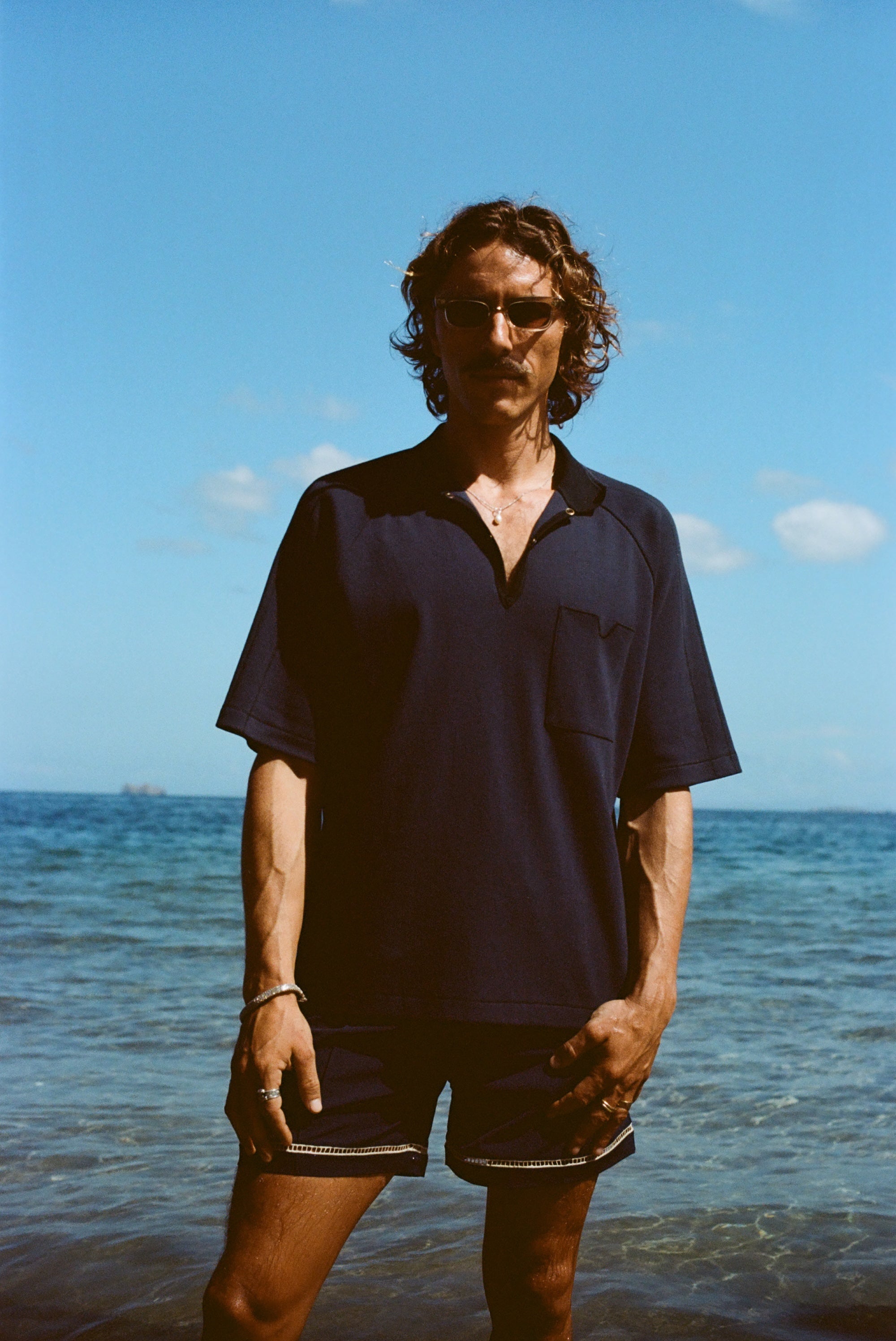 Man posed on the beach wearing navy 'TomPolo' with our navy Cabrisa swim trunks.