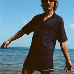 Man posed knee deep in the ocean wearing the navy 'TomPolo' with our navy Cabrisa swim trunks.