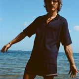 Man posed knee deep in the ocean wearing the navy 'TomPolo' with our navy Cabrisa swim trunks.